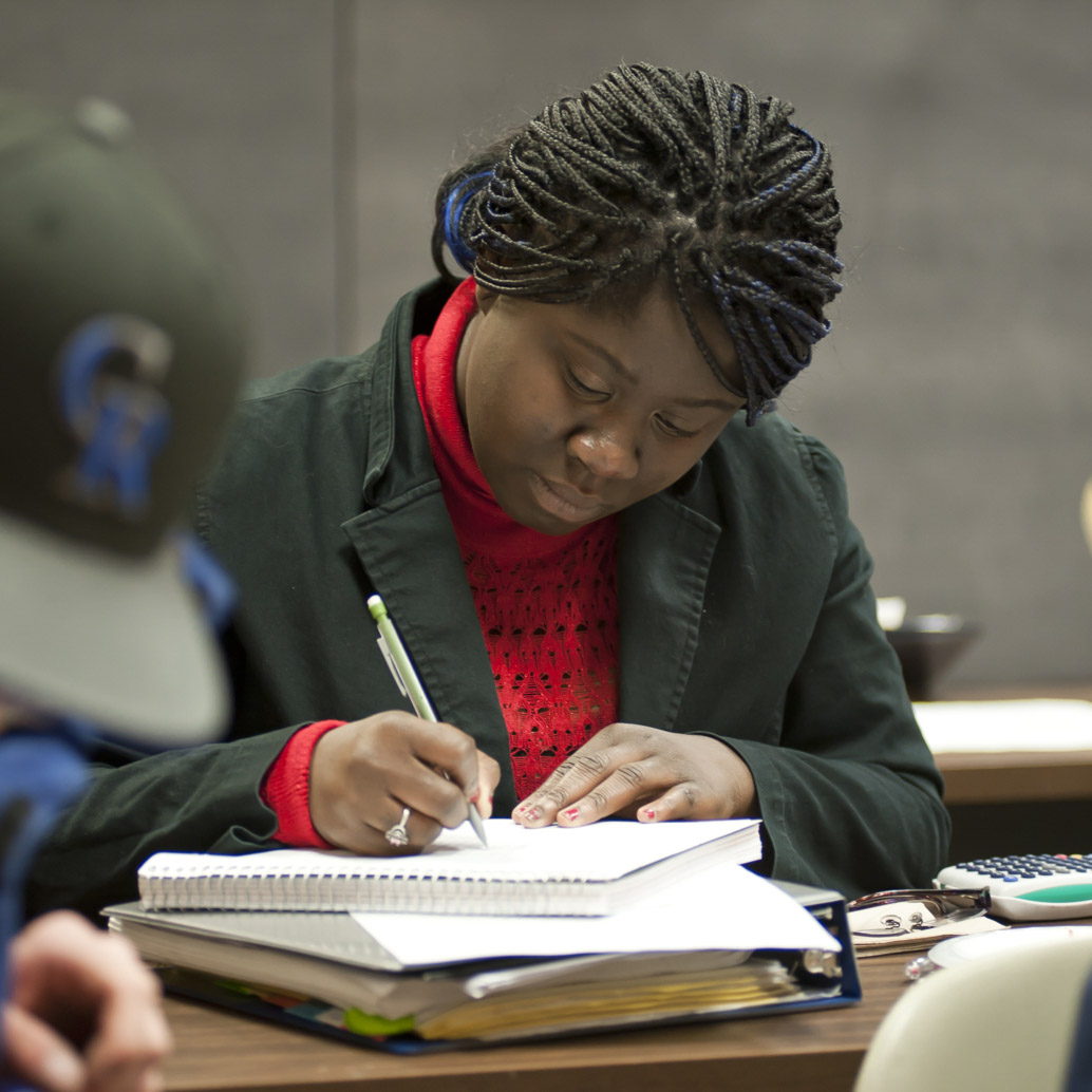 Student writing in a notebook in class. 