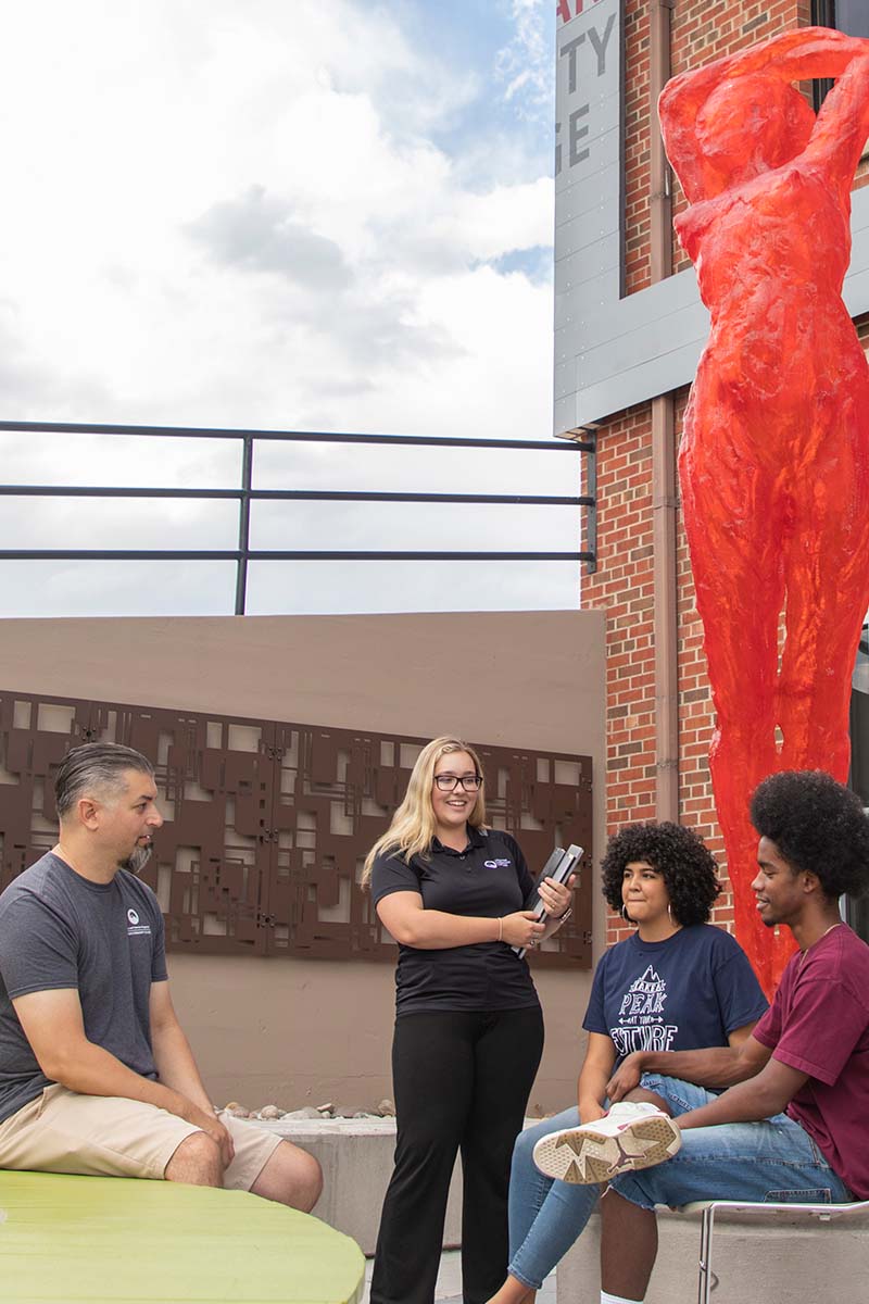 Students sitting or standing in front of a sculpture at the Downtown Studio Campus.