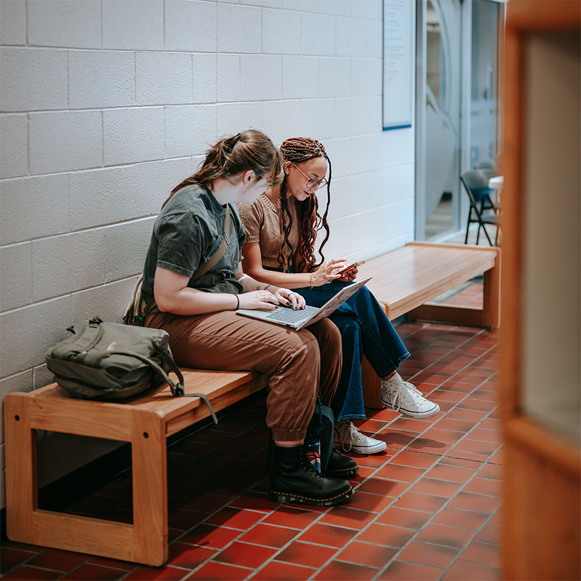 Students in hallway with laptops helping each other